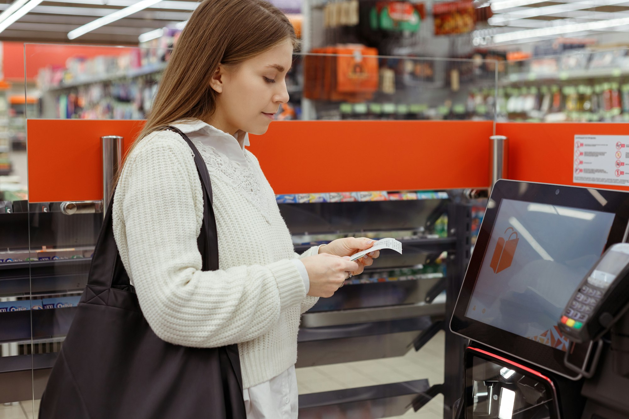 Сustomer woman at self-service checkout in modern supermarket take cash receipt